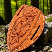 tan leather sheath with floral design and stitching, placed on a stone surface with a natural background.