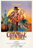 Movie poster for 'Crocodile Dundee' featuring a man with a gun, a woman, and a crocodile.
